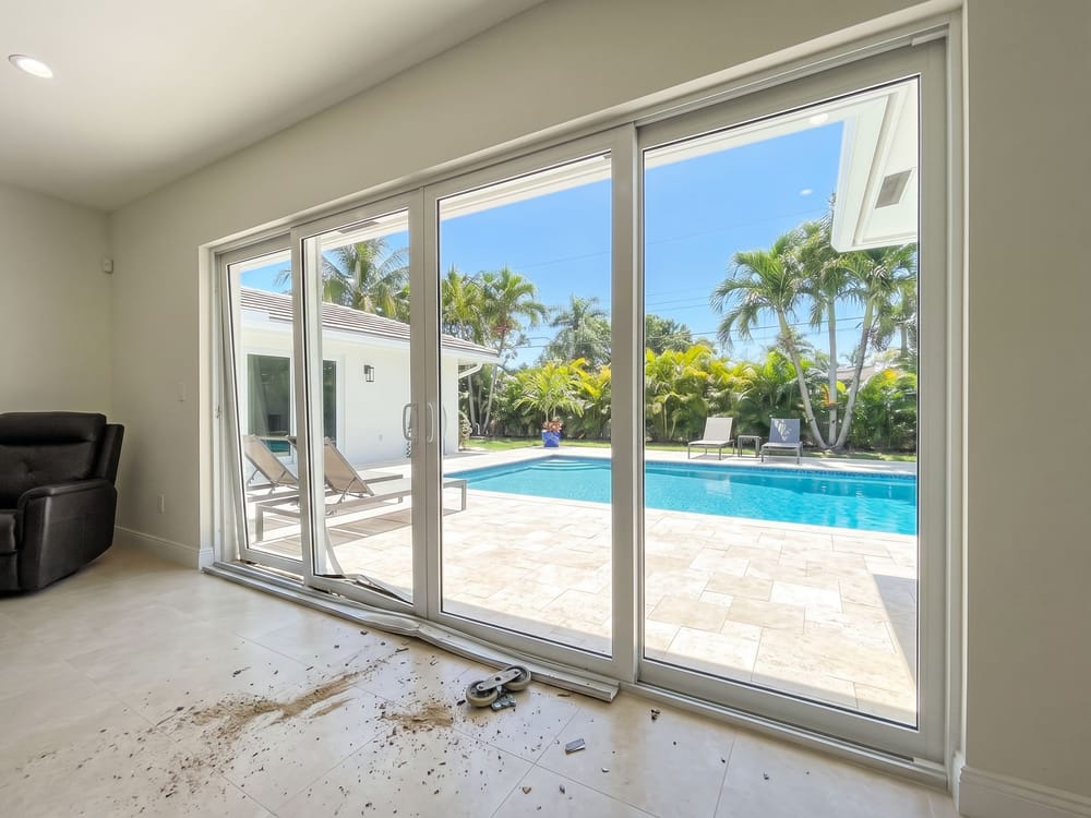 Sliding glass door wall before repair, with a bent bottom track, a roller popped out of its housing and the panel dragging off alignment